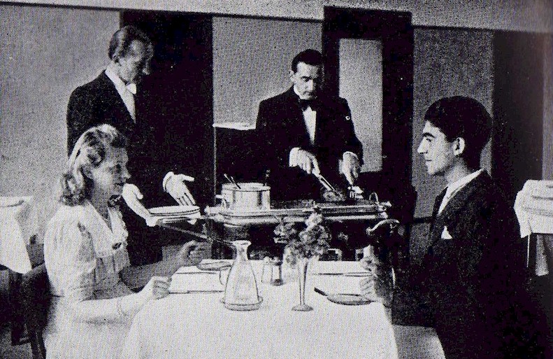 una vecchia foto in bianco e nero il Metre guarda il chef trancheur sta tagliando un arrosto e i due commensali attendono